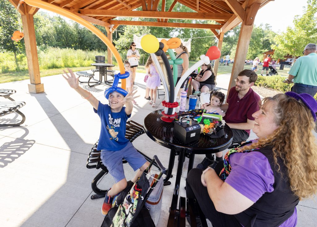 A balloon artist entertains children as a boy reaches for a balloon hat at the Summer BBQ Reunion.