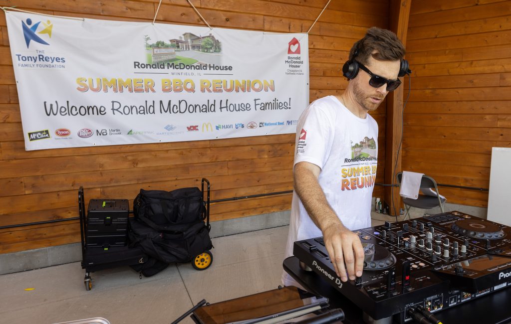 DJ Tsunami plays music beside the Summer BBQ Reunion sponsor banner at Ronald McDonald House Winfield, IL.