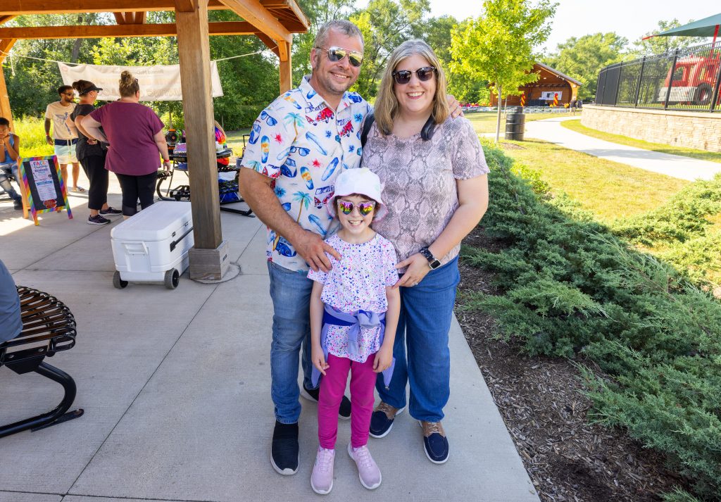 A family of three smiles together at the Ronald McDonald House Summer BBQ Reunion.